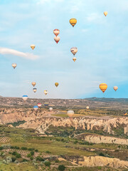 Flying in sky many bright colored beautiful balloons into air in Cappadocia in mountains early at sunrise, dawn. Filling balloon with hot air from burner, big basket. Tourists excursion, cloud flight