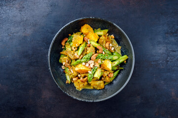 Traditional curry chicken fillet with orange, green asparagus and nuts in sweet sour vinaigrette served as top view in a design plate with text space