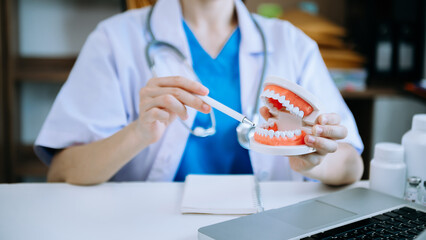 Obraz na płótnie Canvas Concentrated dentist sitting at table with jaw samples tooth model and working with tablet and laptop in dental office professional dental clinic.