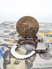 handcuffs and cryptocurrency coin lying on the banknotes of american dollars