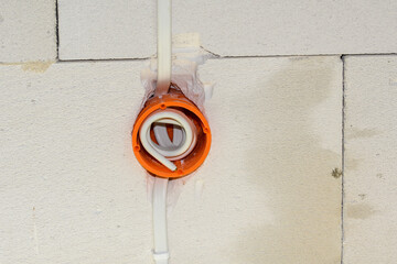 Przewód elektryczny ukryty w ścianie za pomocą pomarańczowej plastikowej puszki elektrycznej.  - obrazy, fototapety, plakaty