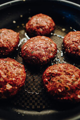 Raw meatballs in a pan while frying