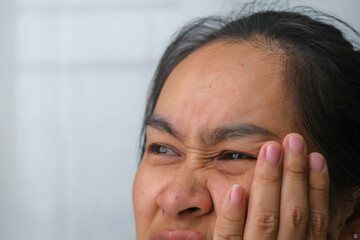 Asian woman holding her hand on her cheek feeling toothache, tooth decay, gingivitis or bad breath problem. Toothache and oral health concept.