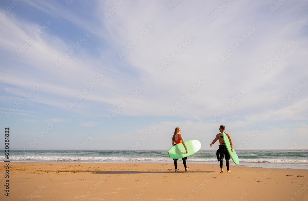 Wall mural Surfing Together. Young Couple With Surfboards Going Into The Ocean, Rear View