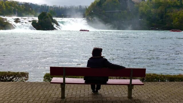 Woman Sitting on a Bench in Front of Rhine Falls at Neuhausen in Schaffhausen, Switzerland.