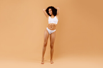 Full length shot of sensual young black lady posing in underwear with hands behind her head,...