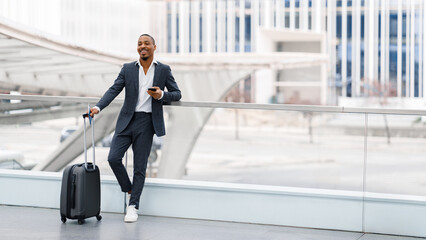 Air Travels. Happy Black Businessman In Suit Standing With Luggage At Airport