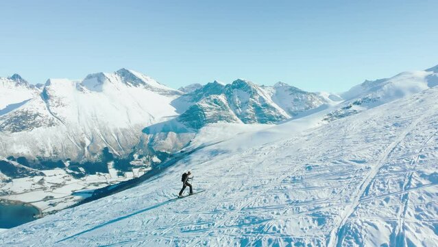Inspiring and cinematic free ride skier concept. Solo backcountry rider slowly walk steep mountain side to approach face. Ski tour in Norwegian fjords. Mountaineering on epic snow mountain.