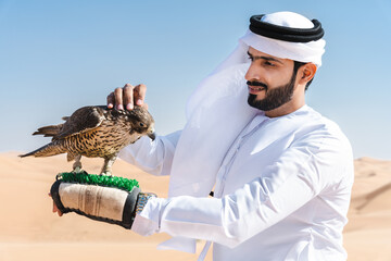 Middle-eastern emirati man wearing arab kandura holding falcon in the desert
