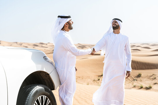Two middle-eastern emirati men wearing arab kandura driving car in the desert