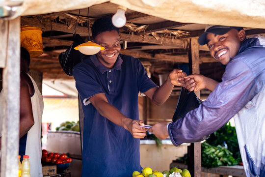 a happy young man selling items to a customer in a neighborhood market.