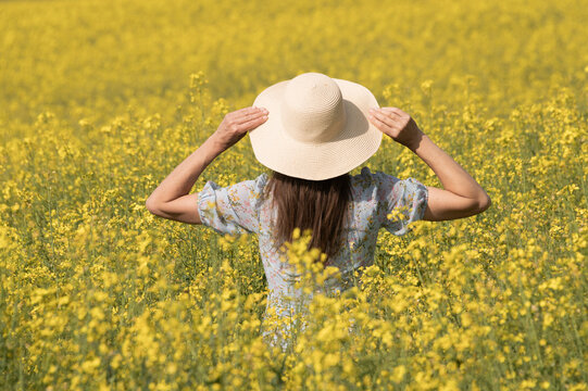 woman with summer hat in a field of yellow rapeseed flowers

