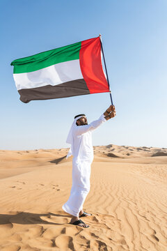 Middle-eastern emirati man wearing arab kandura holding emirati flag in the desert