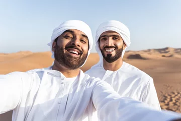 Poster Two middle-eastern emirati men wearing arab kandura bonding in the desert © oneinchpunch