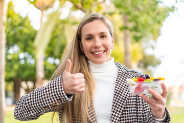 Young blonde woman holding a three dimensional puzzle cube at outdoors with thumbs up because...