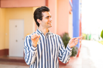 Obraz premium Young handsome man holding home keys at outdoors pointing to the side to present a product