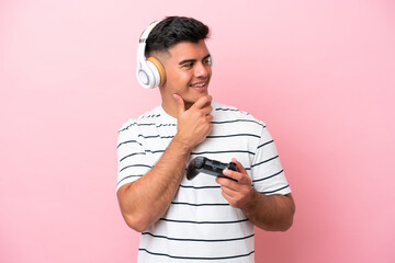 Young handsome man playing with a video game controller isolated on pink background looking to the side and smiling