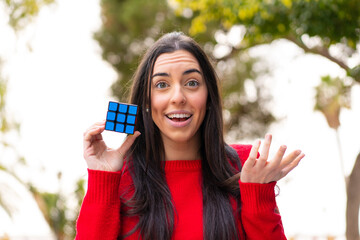 Young woman holding a three dimensional puzzle cube at outdoors with shocked facial expression
