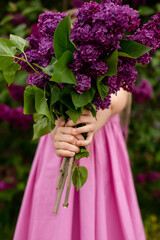 a bouquet of purple lilac in the hands of a girl on the background of a lilac bush spring