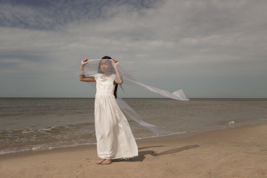girl in white dress dancing with veil on beach
