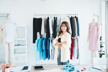 Beautiful designer standing with arms crossed in workshop full of clothes and mannequins.