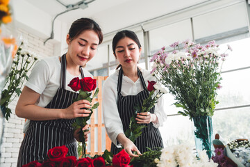 Two female employees meticulously trim flowers to be delivered to customers in a flower shop.