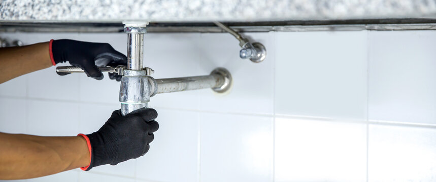 Technician plumber using a wrench to repair a water pipe under the sink. Concept of maintenance, fix water plumbing leaks, replace the kitchen sink drain, cleaning clogged pipes is dirty or rusty.