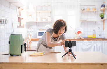 Portrait of asian chef girl cooking potato fried by Air Fryer machine in kitchen home with live camera. Work at home lifestyle. Technology eco friendly home smart device, asian housewife, minimal life