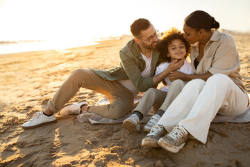 Happy family concept. Multiracial parents and their son sitting on the beach, enjoying and spending time on coastline