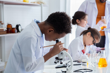 Selective focus of boy student in gown uniform research using microscope equipment and tube,...