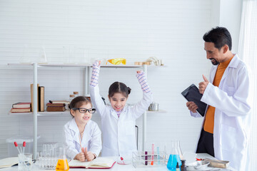 Science teacher and elementary pupils in white gowns workshop training in chemistry classroom, kids studying an experiment in laboratory, scientist students using pipette dropping liquid to test tube