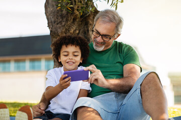 Happy old european grandfather and mixed race little boy have fun in park enjoy free time together