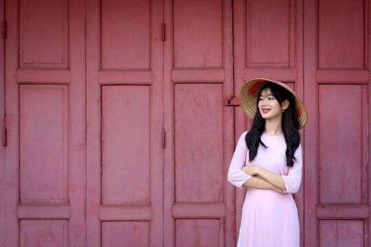A pretty Vietnamese young Asian girl wearing an Ao Dai a traditional Vietnam dress national costume color pink with an old red door.