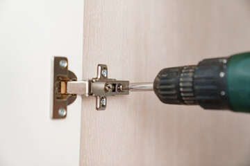 The master adjusts the furniture hinge on the cabinet door with a screwdriver.