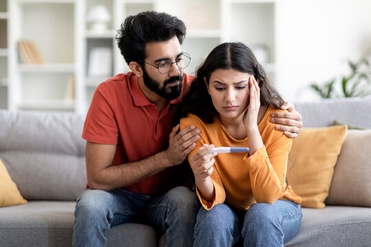 Infertility Problems. Portrait Of Upset Indian Couple Looking At Negative Pregnancy Test