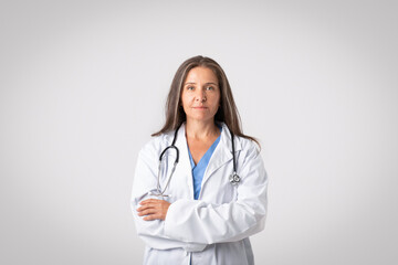 Fototapeta premium The face of modern healthcare. Portrait of confident senior doctor woman posing with folded arms, light background