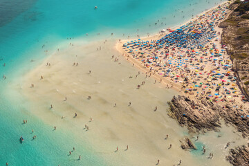 Aerial view of blue sea and sandy beach with umbrellas and crowd of people at sunrise in summer. Beautiful landscape with sea coast and swimming people and and turquoise water. Top view