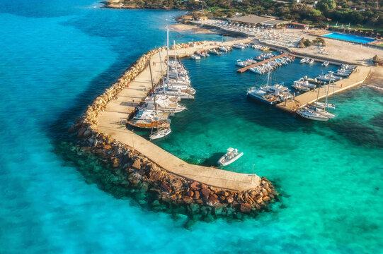 Top view colorful seascape with sailboats and motorboats in sea bay top view. Aerial view of boats and luxury yachts in dock at dawn in summer in Sardinia, Italy. Travel background, clear sea