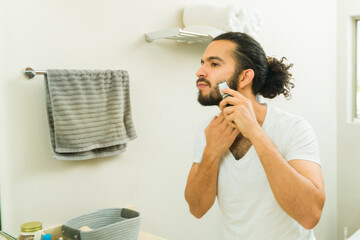 Young man with a beard using a trimmer in the bathroom