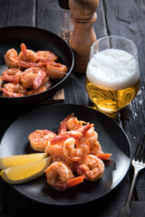 Fried Argentinean prawns on a black plate with lemon and a glass of beer on a dark wooden table.