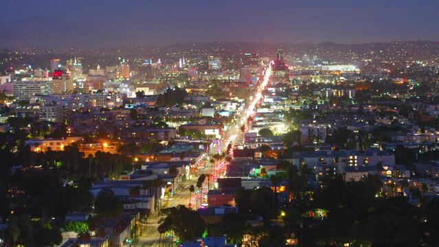 Aerial Panning Shot Of Vehicles Amidst Buildings In Illuminated City Against Sky At Night - Los Angeles, California