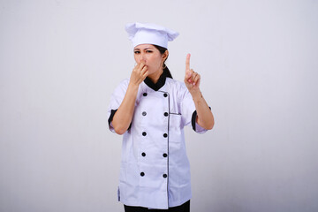 Photo of disappointed and unhappy female Asian chef standing with hand covering nose, bad smell gesture, feeling disgusted on empty space or copy space for product isolated on white background