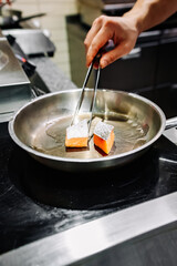 man chef cooking fried salmon fish in frying pan on kitchen