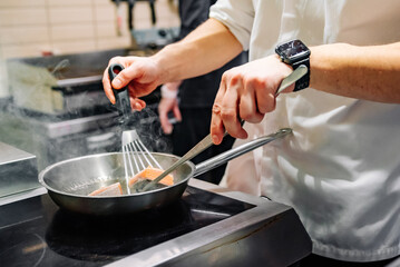 man chef cooking fried salmon fish in frying pan on kitchen
