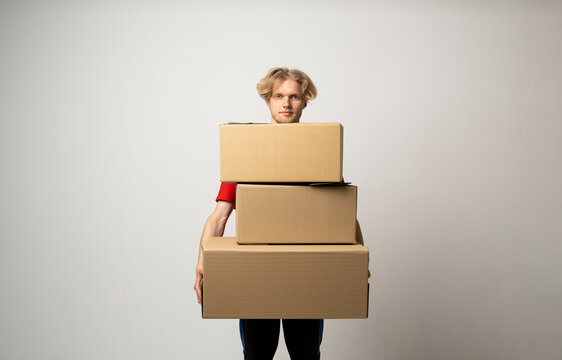 Young delivery man standing with lot of parcel post boxes isolated over white background.