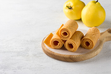 Natural quince pastille on a wooden board surrounded by fresh quince fruits on a light gray background