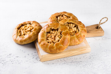 Sweet mini pies with apples and cinnamon on a wooden board on a light gray background. Delicious homemade food