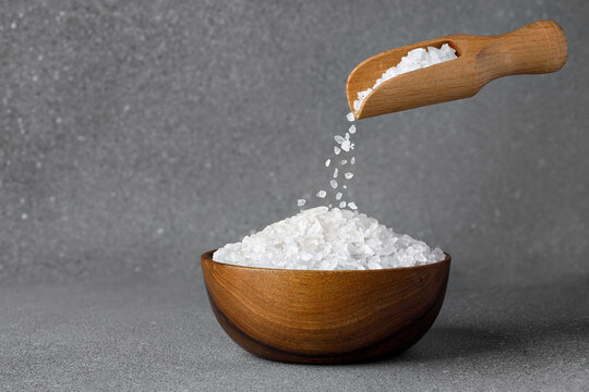 sea salt crystals falling from scoop in bowl on grey background