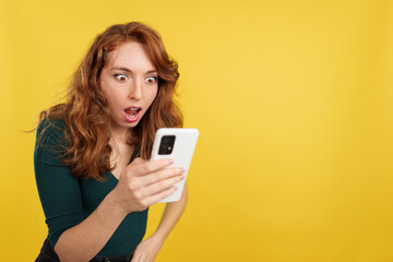 Surprised redheaded woman looking the screen of a mobile