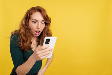 Naklejka premium Surprised redheaded woman looking the screen of a mobile